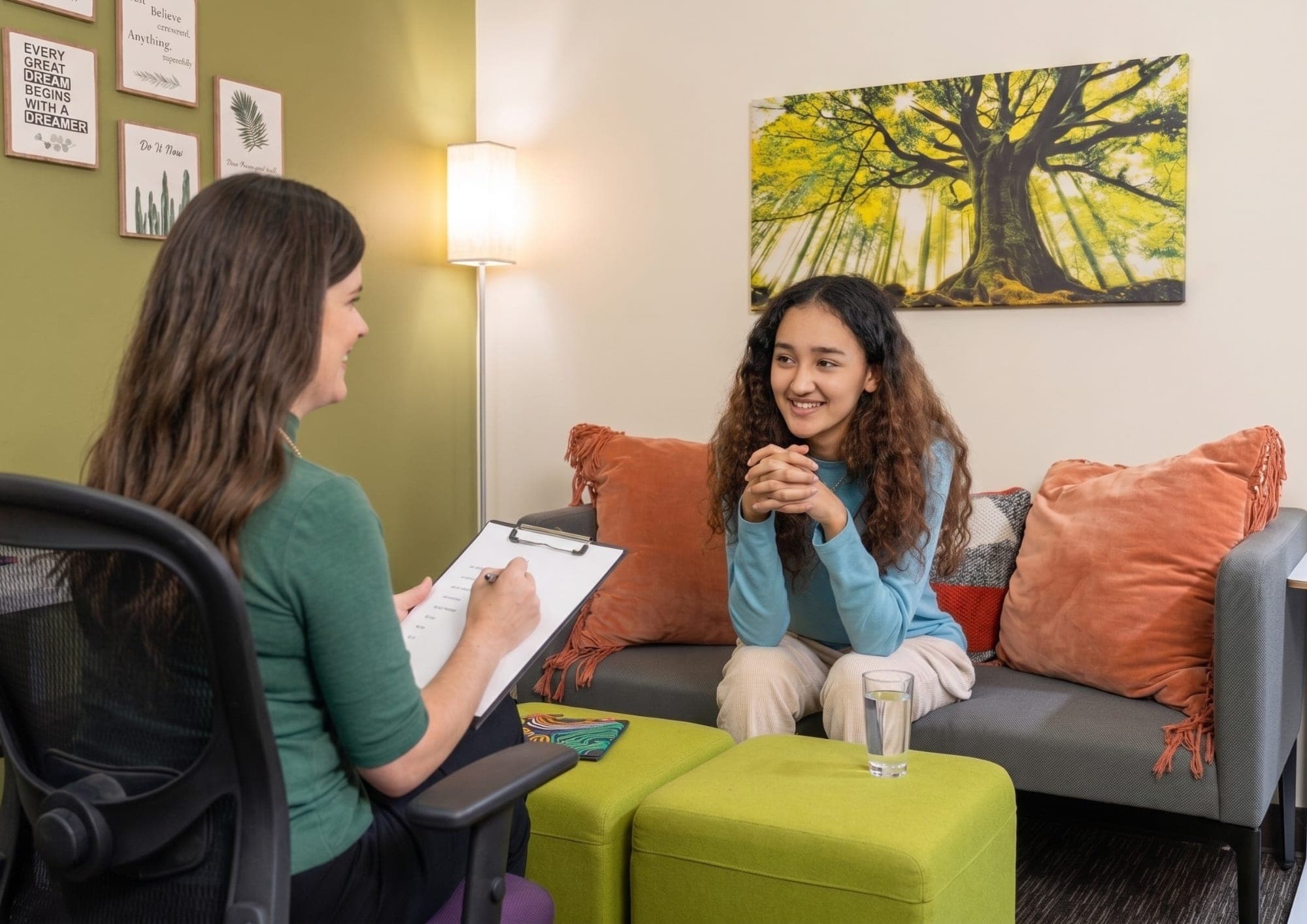 A teenager sitting on a couch in the practice’s Mesa room, smiling in conversation with a clinician who is making notes on a clipboard.